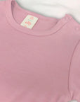 Close-up of a pink baby onesie with a visible brand label on a light gray background