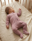 Baby in a pink sleepsuit lying on a crib with white bedding