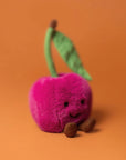 Amuseables Cherry plush toy angled on orange background with smiling face