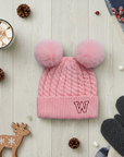 Pink knitted beanie with double pom-poms on a flat lay