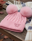 Pink knitted beanie with double pom-poms on an autumn table