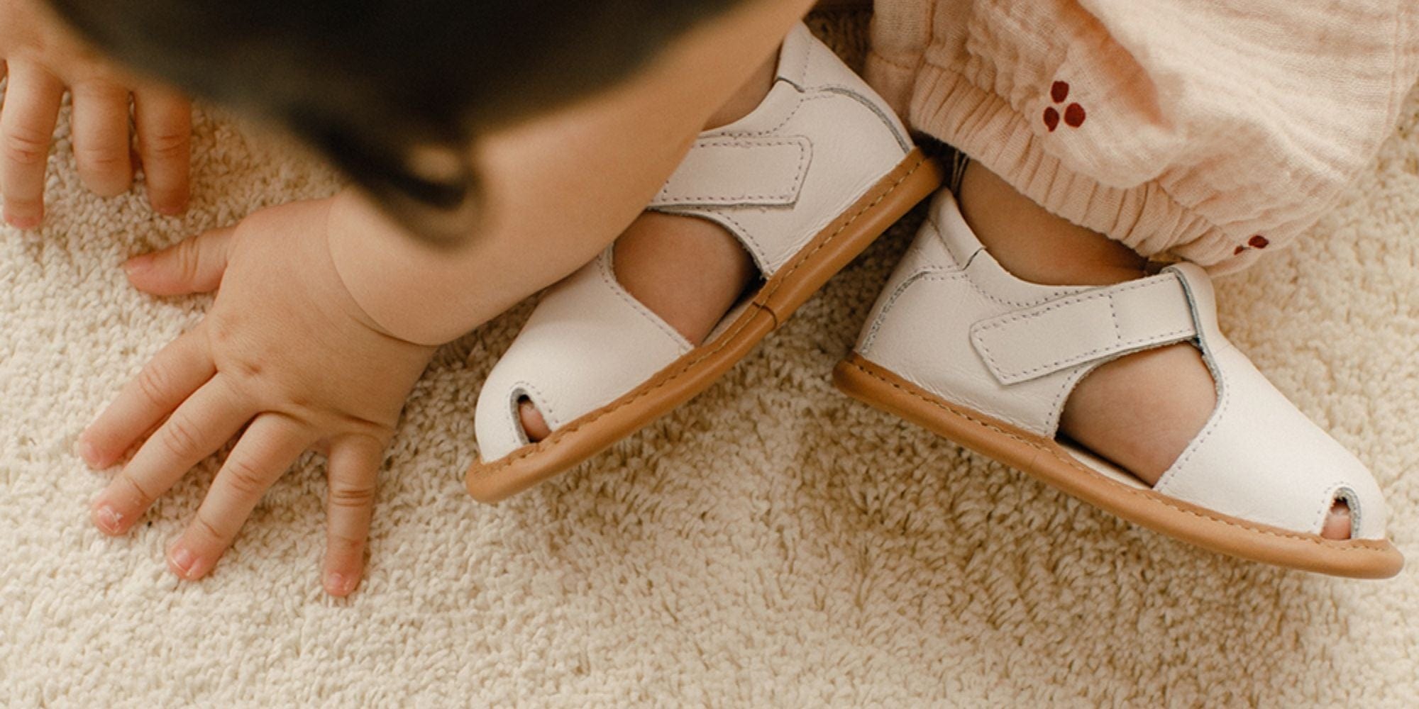 TTJ Baby wearing white sandals on carpet