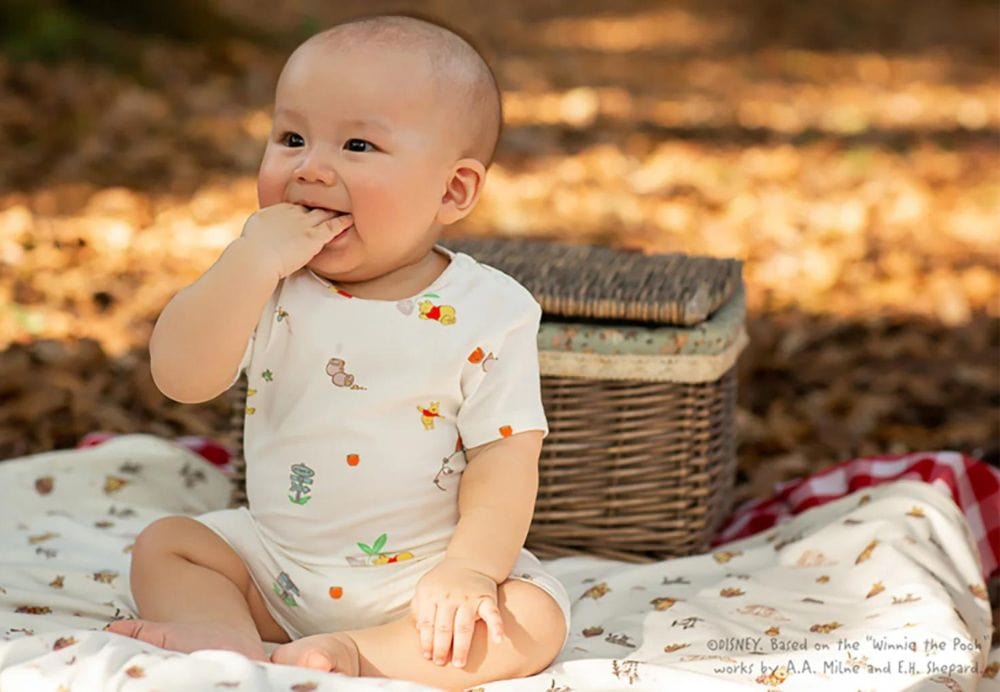 Baby in new clothing collection, smiling near picnic basket.