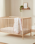 Wooden crib with a white mattress and pink blanket in a nursery setting.