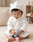 White bear hooded baby bathrobe with personalised name, baby sitting on soft rug holding toy