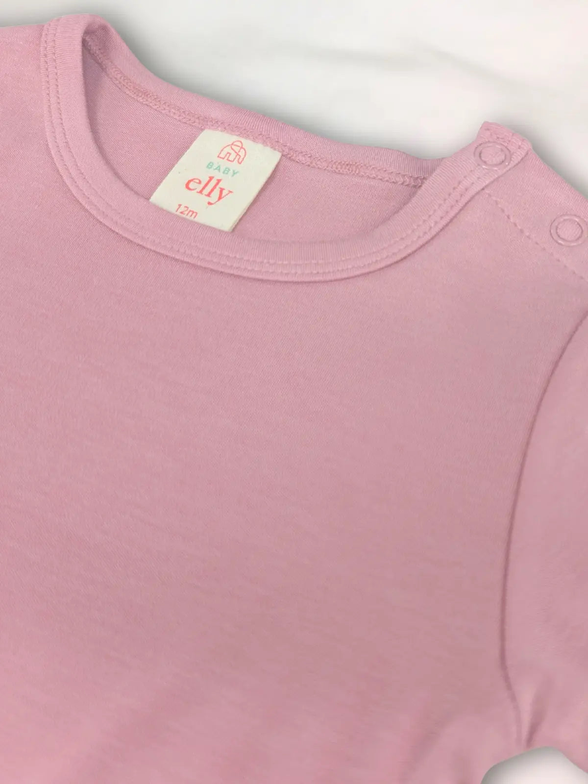 Close-up of a pink baby onesie with a visible brand label on a light gray background