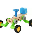 A wooden toy vehicle with bright green chassis, natural wood body, black wheels with yellow rims, and blue steering wheel and dashboard, shown on a white background.