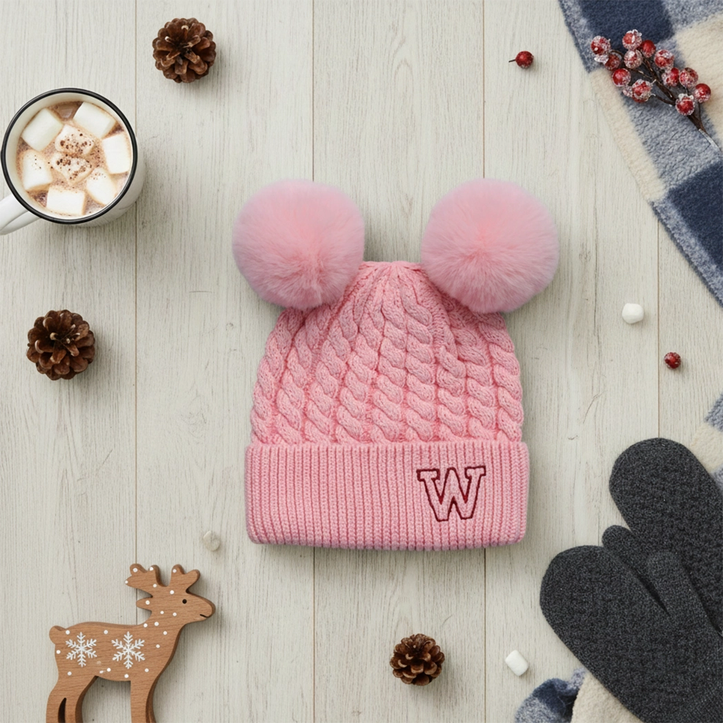 Pink knitted beanie with double pom-poms on a flat lay