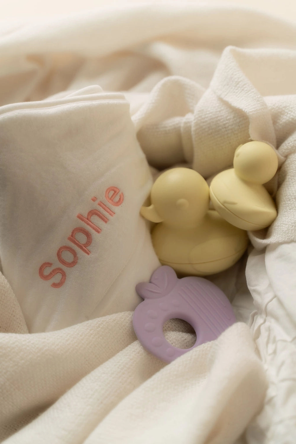 Yellow duck and purple teether on a white blanket with 'sophie' embroidered.