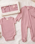 Pink baby bodysuit and onesie set on a light background