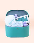 A teal vegan leather keepsake trunk open to reveal a personalized baby gift set including a white blanket, teal clothing, and purple rubber ducks.