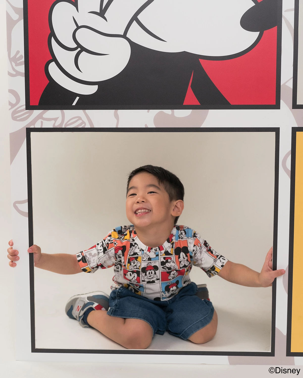 Child in pop comic mickey tee in front of a large Mickey Mouse poster