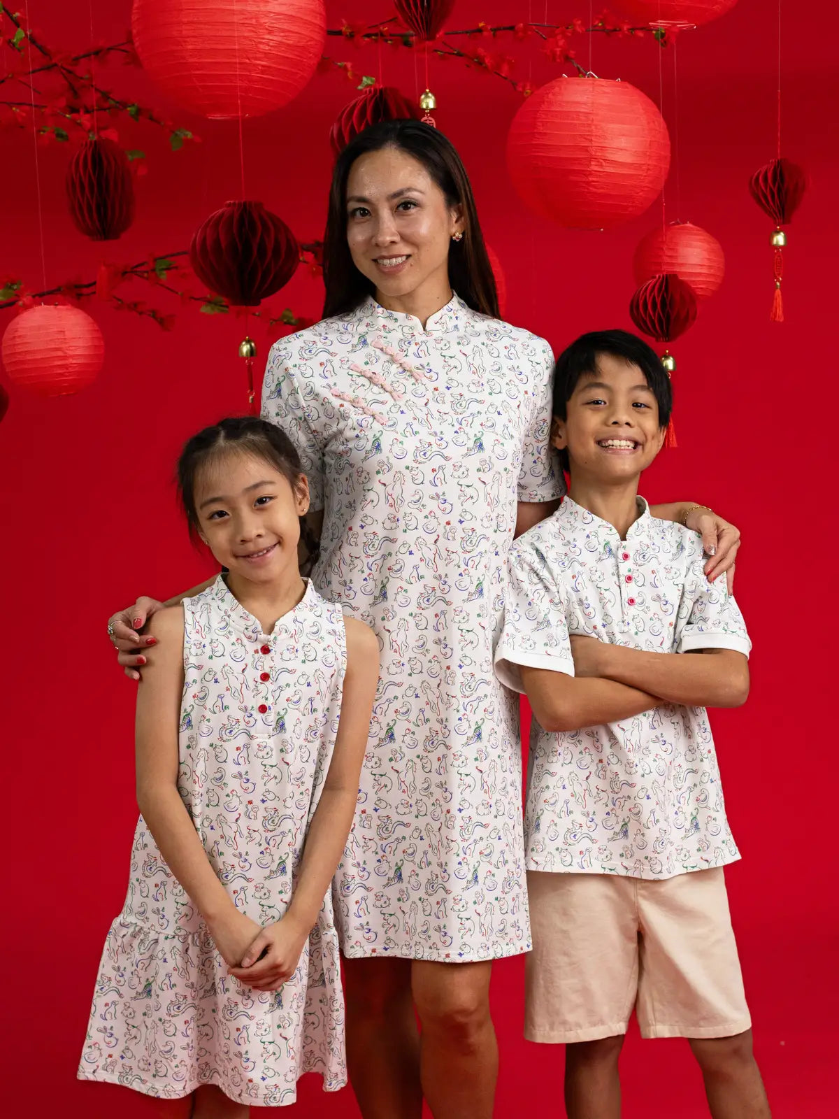 Three kids in matching Elly Zodiac Mahjong outfits against a red background.