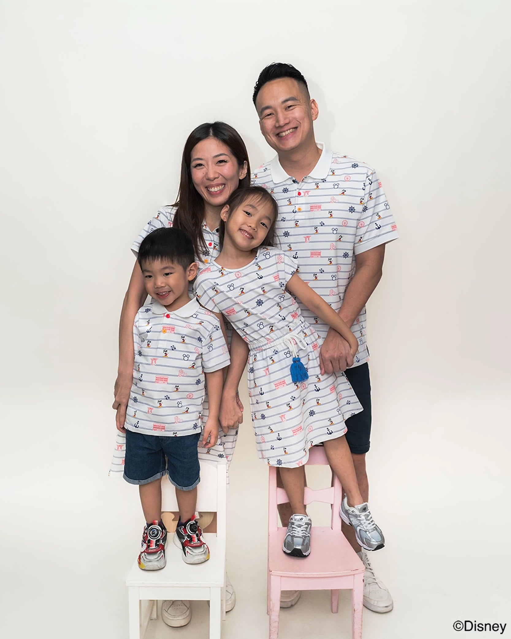Family of four wearing matching sailor mickey stripes outfits with a white background