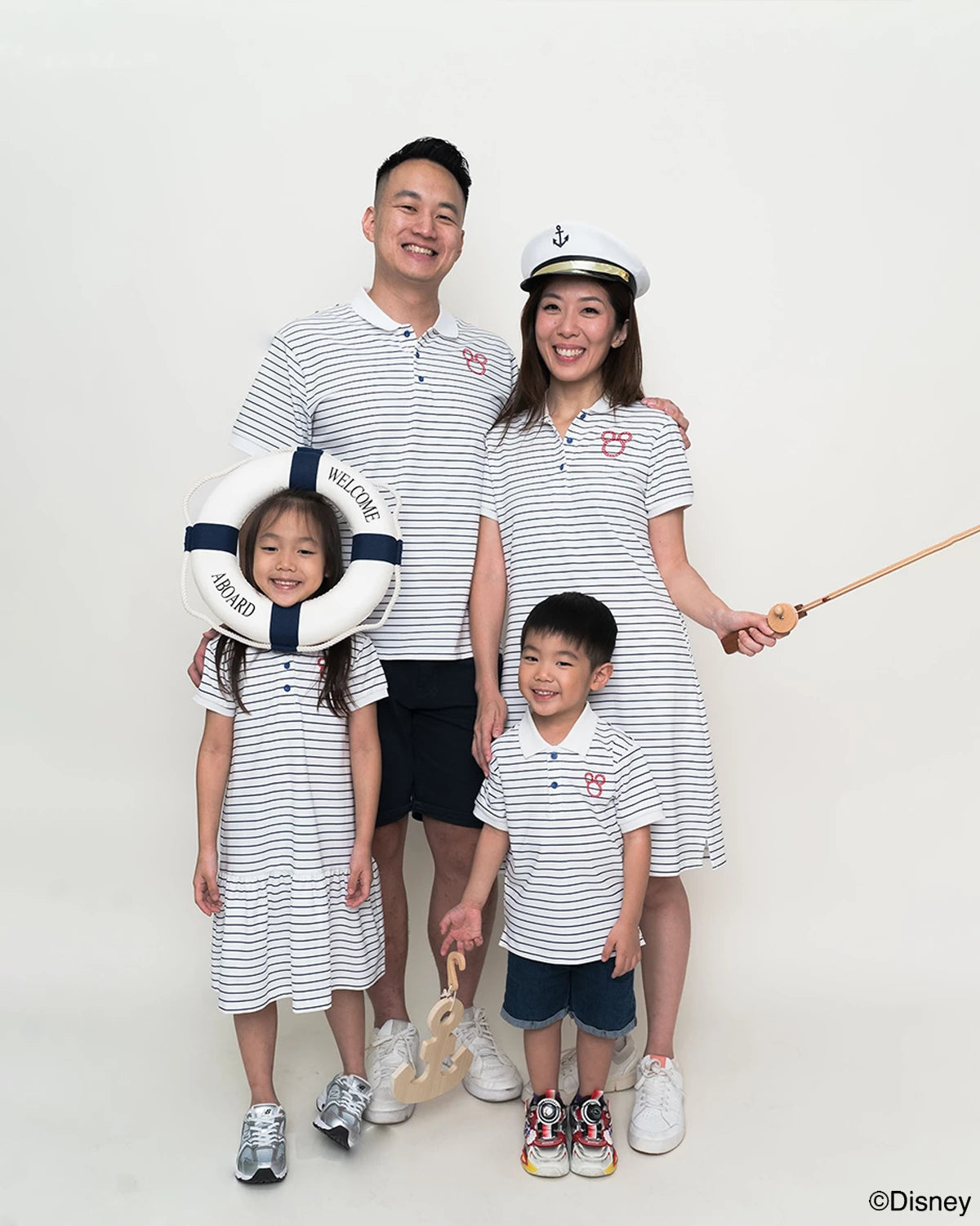 Family of four wearing matching sailor mickey stripes outfits with a white background