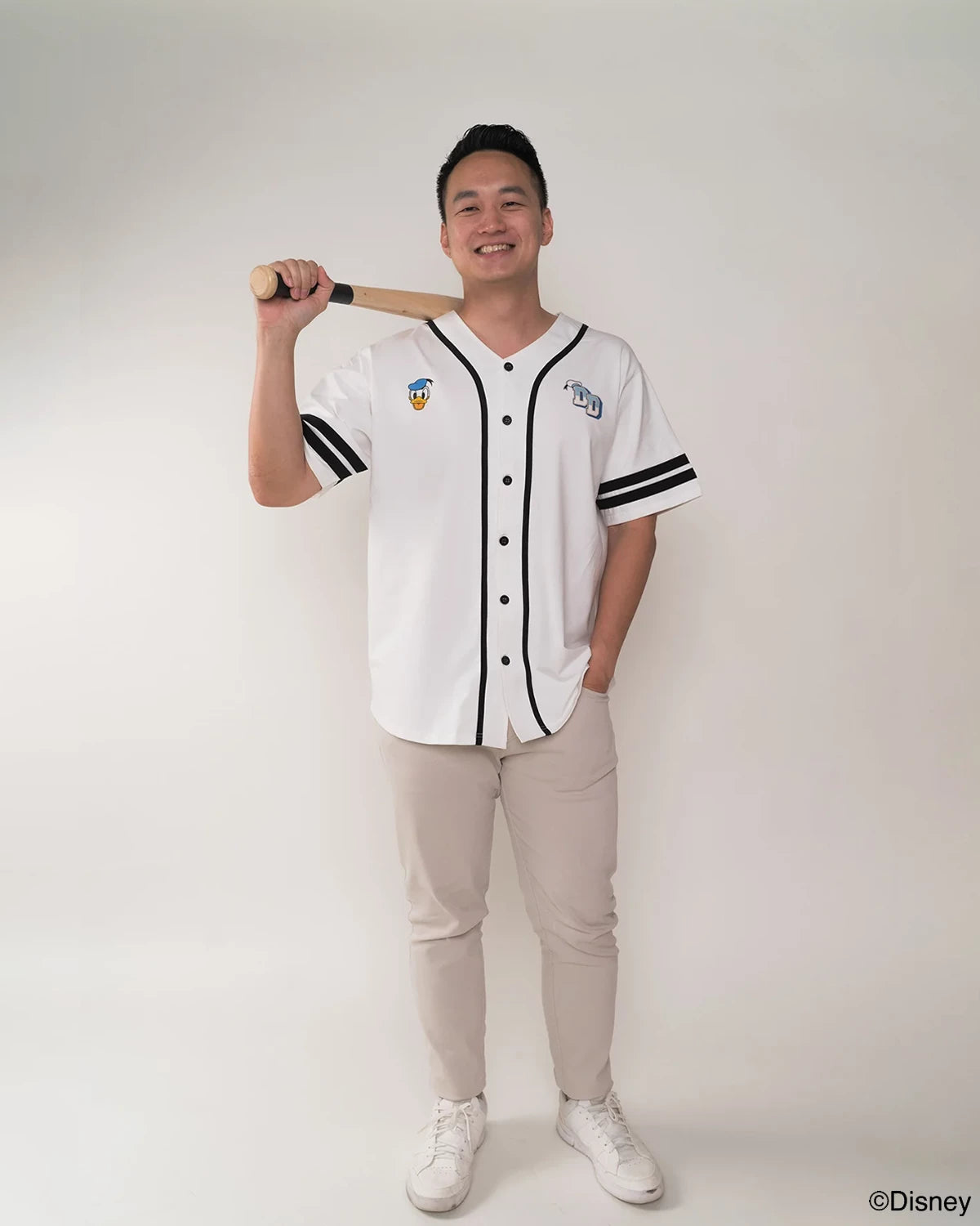 Person wearing a white baseball jersey with black accents, holding a bat on a plain background.