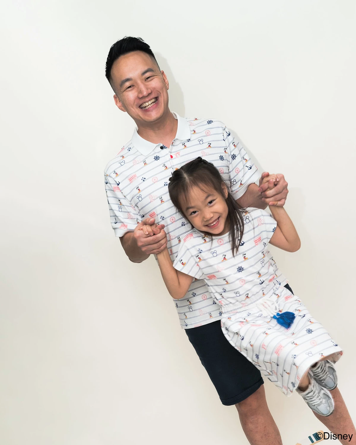 Man and young girl wearing matching nautical mickey outfits  against a white background