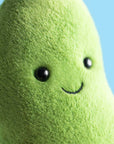 Plush greenbean toy with a smiling face against a blue background