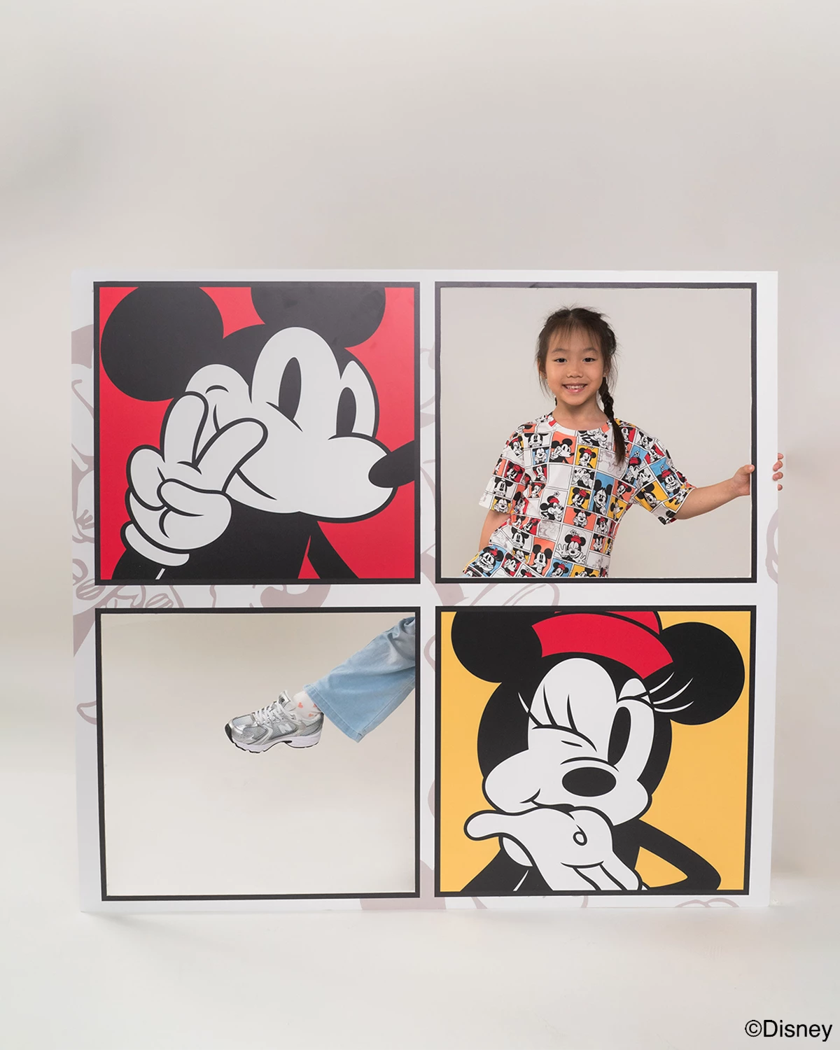 Child wearing pop comic mickey tee and holding up four framed Disney character posters on a white wall.
