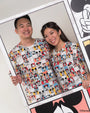 Two people wearing matching adult pop comic mickey tee standing next to a large poster with Mickey Mouse designs.