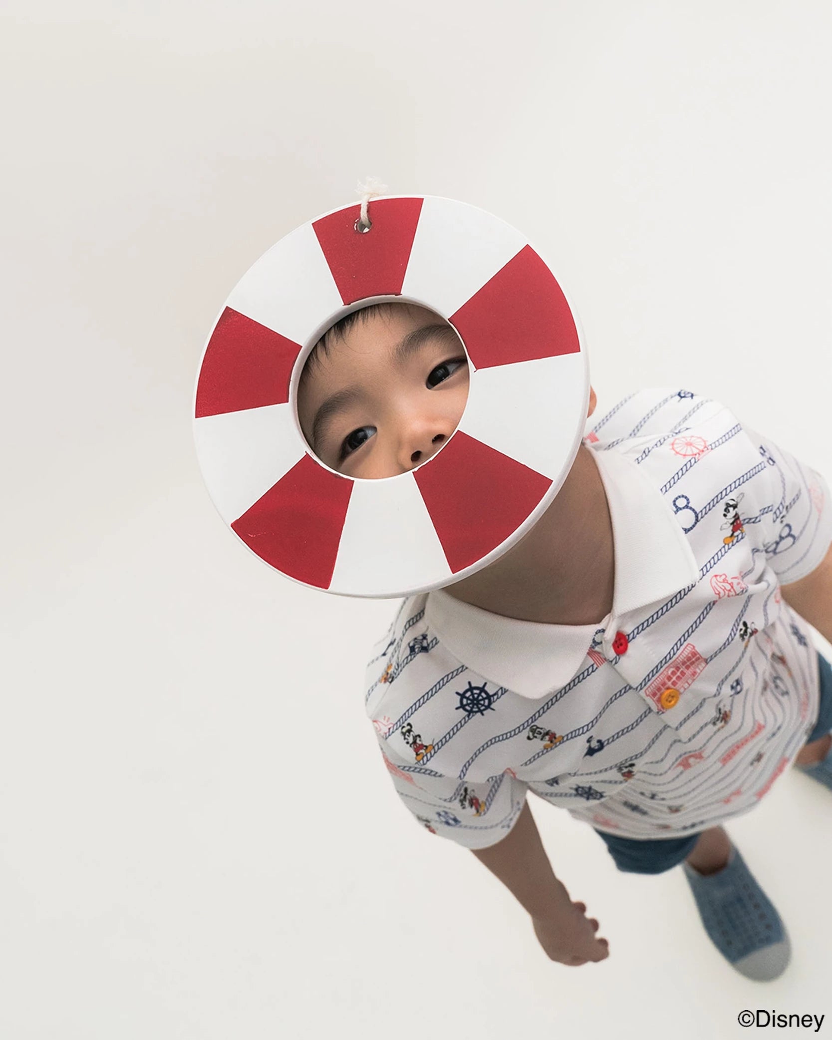 Child wearing stripes sailor mickey polo tee and a red and white life buoy with a white background