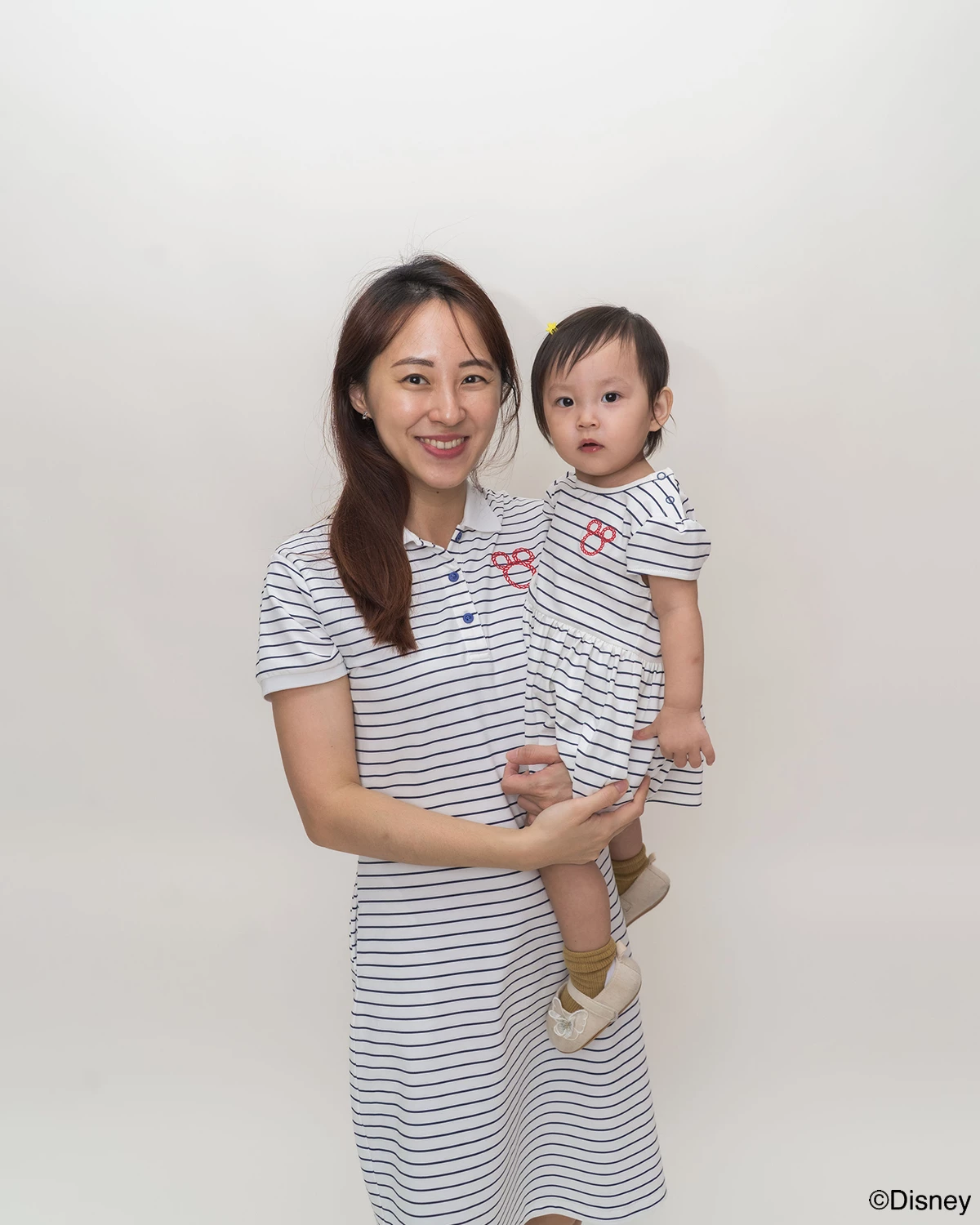 Woman holding a child both wearing matching stripes sailor mickey design  against a plain background